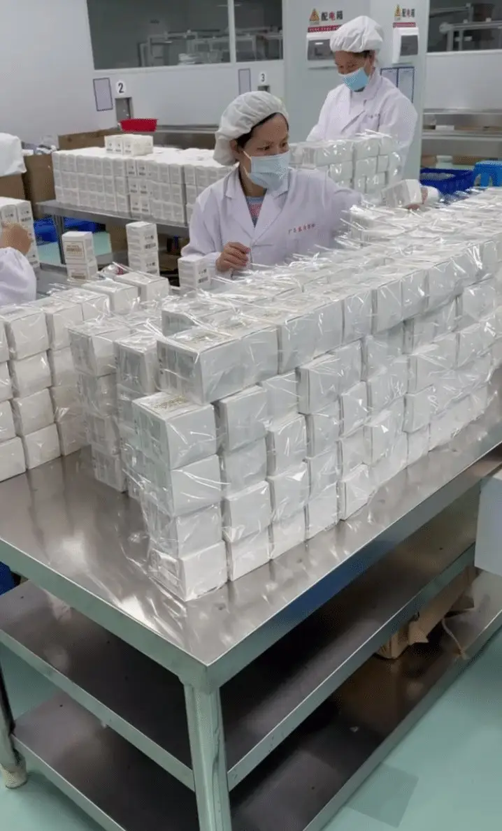 Workers at a factory in China packing cosmetic products into white boxes on a stainless steel table